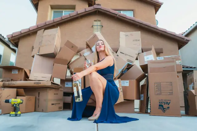 Woman in a blue dress in front of a house and a pile of moving boxes